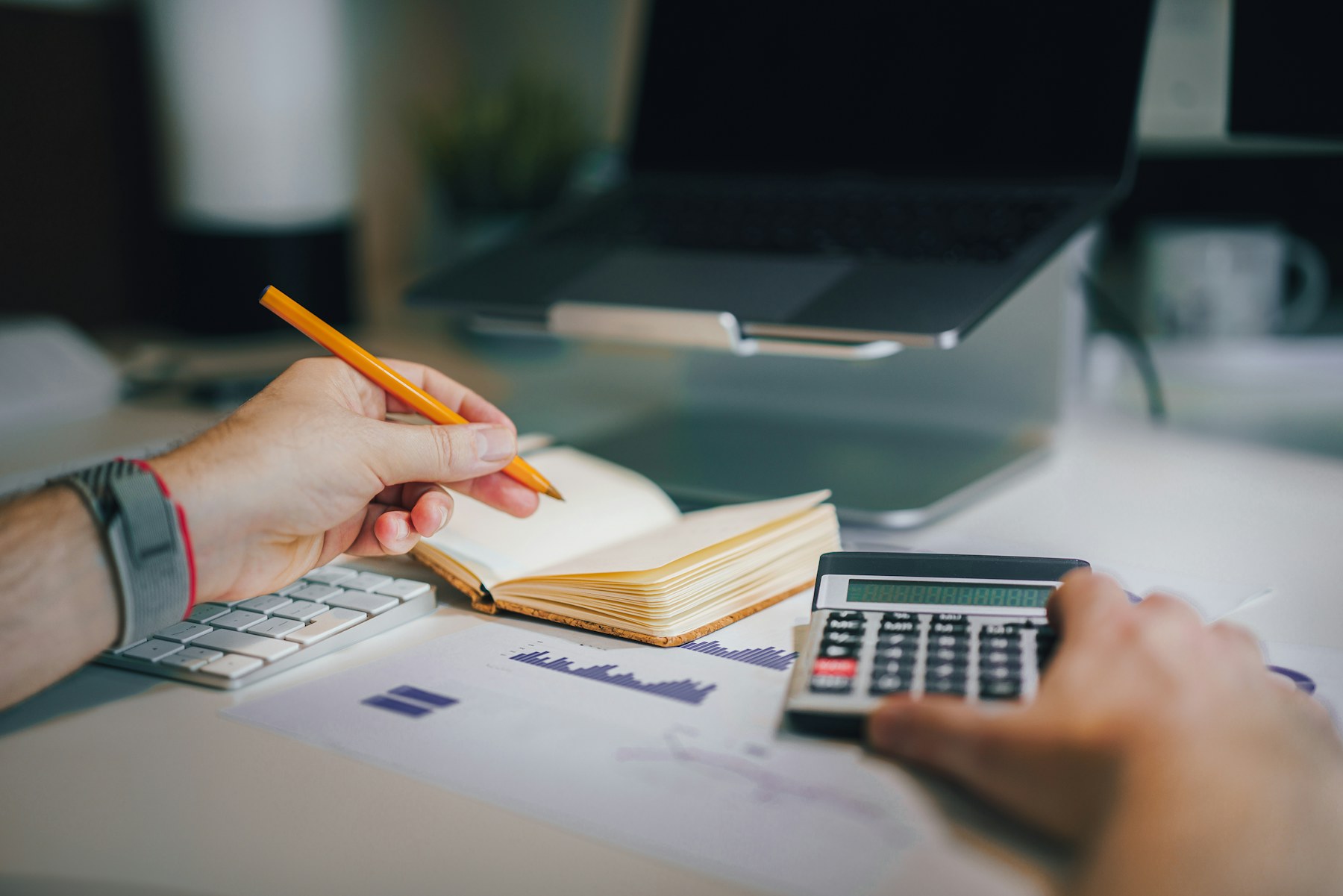 A person recording figures beside a calculator and notebook